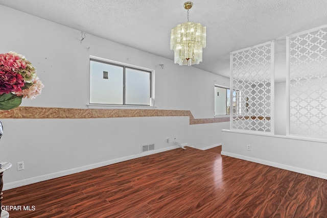 empty room featuring a chandelier, a textured ceiling, and hardwood / wood-style flooring