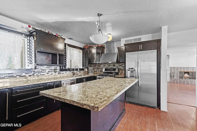 kitchen featuring backsplash, wall chimney range hood, a center island, hanging light fixtures, and stainless steel appliances