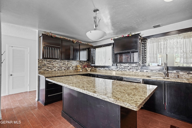 kitchen featuring backsplash, a kitchen island, sink, hanging light fixtures, and light stone countertops