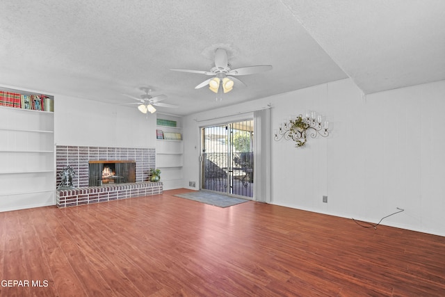 unfurnished living room with ceiling fan, hardwood / wood-style floors, a tiled fireplace, a textured ceiling, and built in shelves