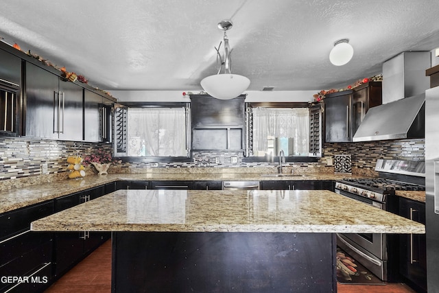 kitchen featuring pendant lighting, a center island, wall chimney range hood, stainless steel appliances, and sink