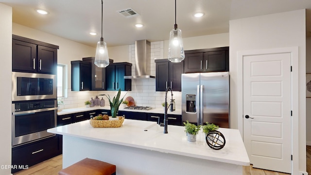 kitchen featuring a center island with sink, visible vents, light countertops, appliances with stainless steel finishes, and wall chimney range hood