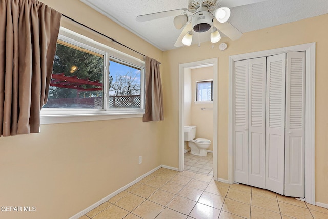 unfurnished bedroom with ceiling fan, a textured ceiling, ensuite bathroom, and light tile patterned flooring