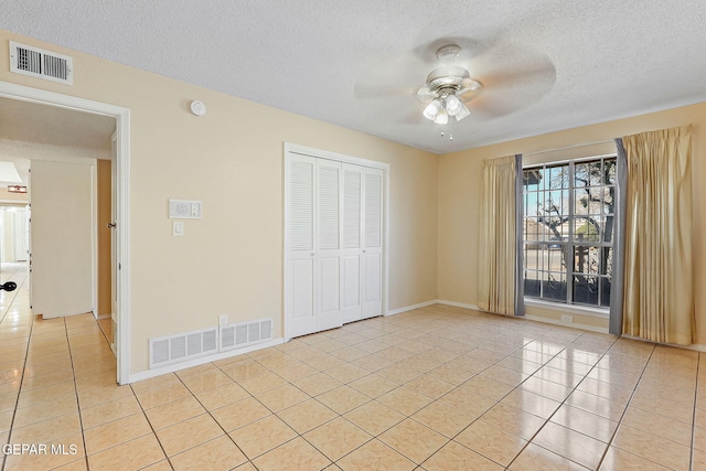 unfurnished bedroom with ceiling fan, light tile patterned floors, a closet, and a textured ceiling