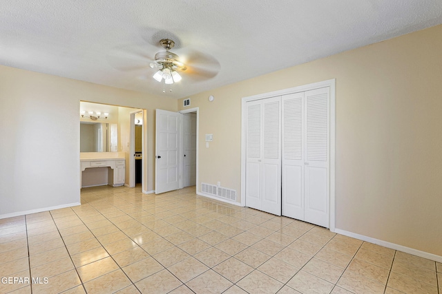 unfurnished bedroom with a textured ceiling, connected bathroom, a closet, light tile patterned flooring, and ceiling fan