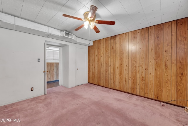 unfurnished room featuring light colored carpet, wood walls, and ceiling fan