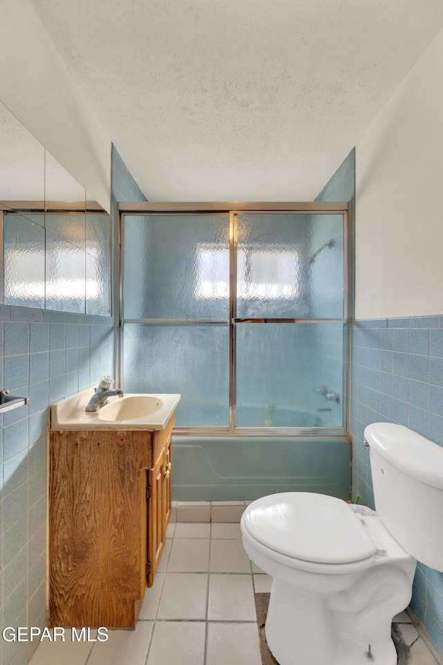 full bathroom featuring toilet, vanity, tile patterned floors, tile walls, and bath / shower combo with glass door