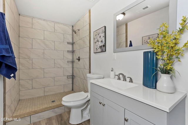 bathroom with toilet, vanity, hardwood / wood-style floors, and a tile shower