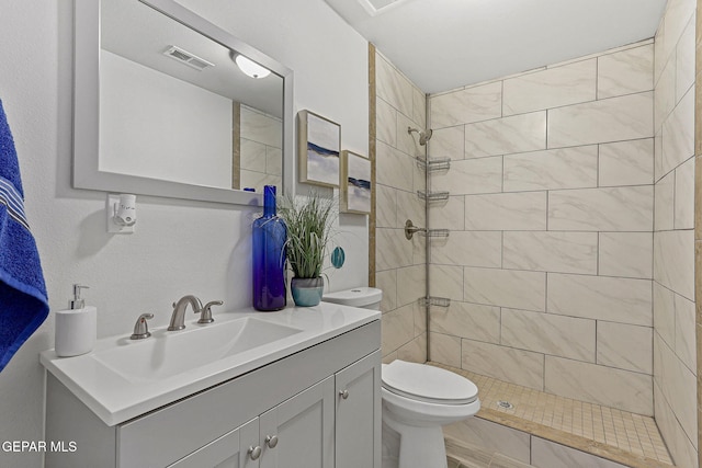 bathroom with toilet, vanity, and a tile shower