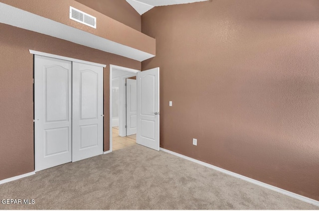 unfurnished bedroom with lofted ceiling, a closet, and light carpet