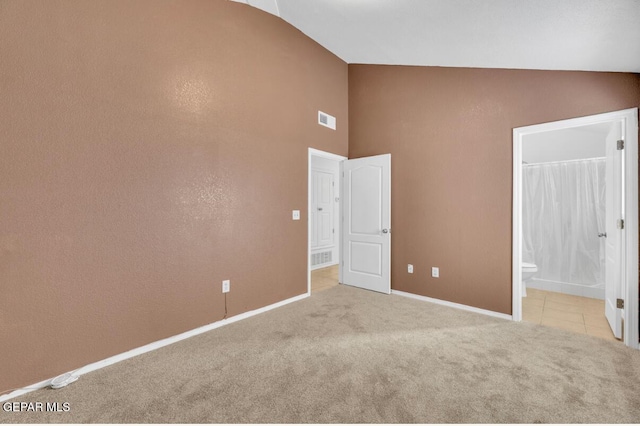 unfurnished bedroom featuring ensuite bath, light carpet, and lofted ceiling