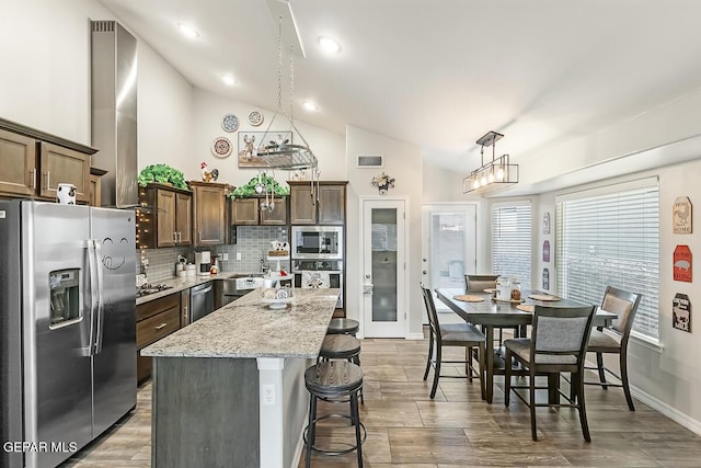 kitchen with appliances with stainless steel finishes, a center island, decorative light fixtures, a kitchen breakfast bar, and vaulted ceiling