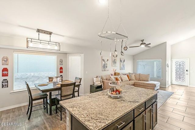 kitchen featuring ceiling fan, dark brown cabinets, light stone countertops, vaulted ceiling, and a kitchen island