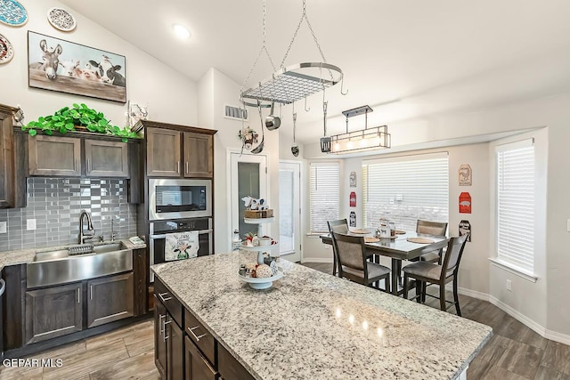 kitchen with lofted ceiling, wood-type flooring, stainless steel oven, built in microwave, and dark brown cabinets