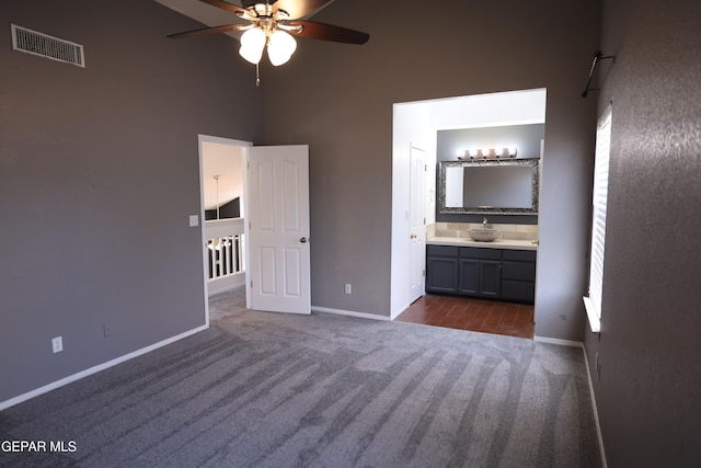 unfurnished bedroom with ceiling fan, dark colored carpet, ensuite bath, a towering ceiling, and sink