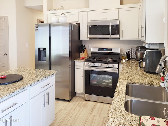 kitchen featuring light stone counters, sink, white cabinets, and stainless steel appliances