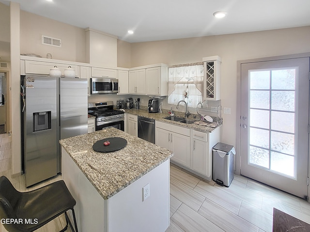 kitchen featuring white cabinetry, appliances with stainless steel finishes, sink, light stone countertops, and a center island