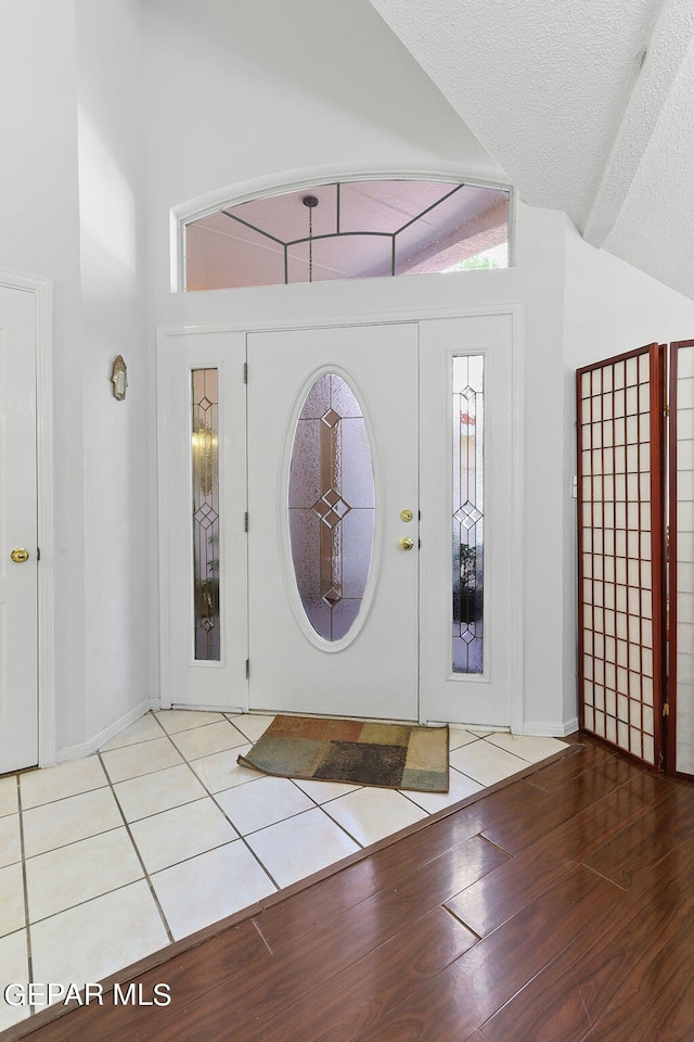 foyer with a textured ceiling, high vaulted ceiling, wood finished floors, and baseboards