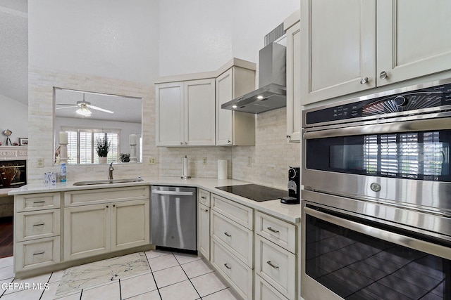 kitchen featuring a sink, a ceiling fan, appliances with stainless steel finishes, wall chimney range hood, and backsplash