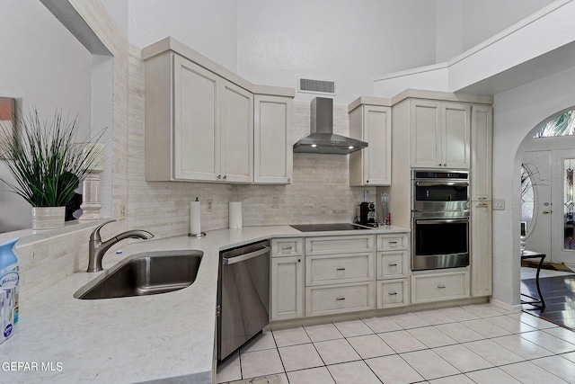 kitchen with arched walkways, a sink, visible vents, appliances with stainless steel finishes, and wall chimney exhaust hood