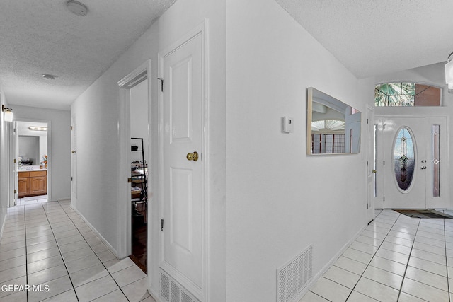 foyer entrance featuring a textured ceiling, light tile patterned flooring, visible vents, and baseboards