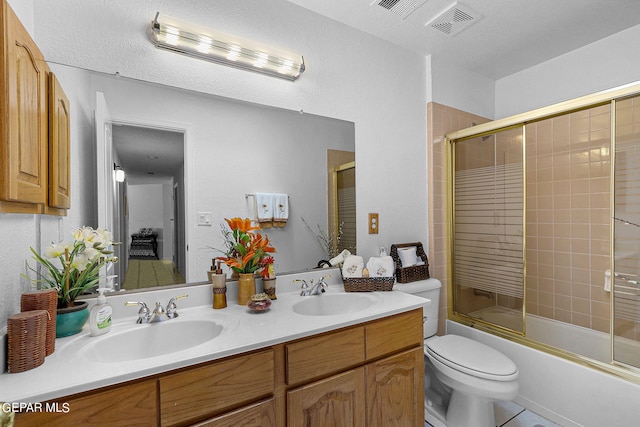 bathroom with double vanity, bath / shower combo with glass door, toilet, and a sink