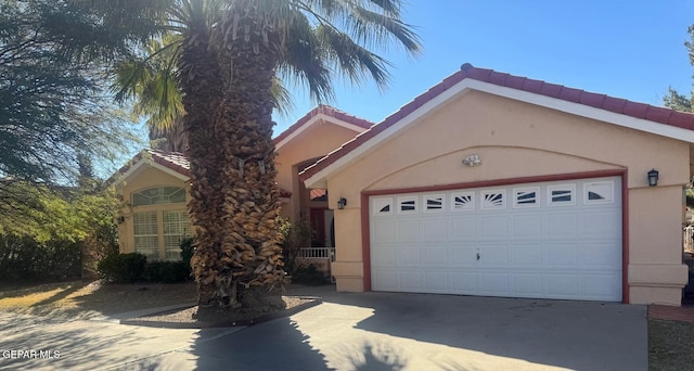 view of front facade featuring driveway, an attached garage, a tiled roof, and stucco siding