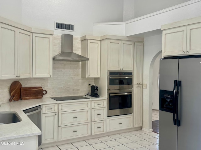 kitchen featuring arched walkways, stainless steel appliances, visible vents, backsplash, and wall chimney range hood