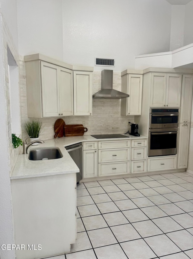 kitchen featuring stainless steel appliances, a high ceiling, a sink, backsplash, and wall chimney exhaust hood