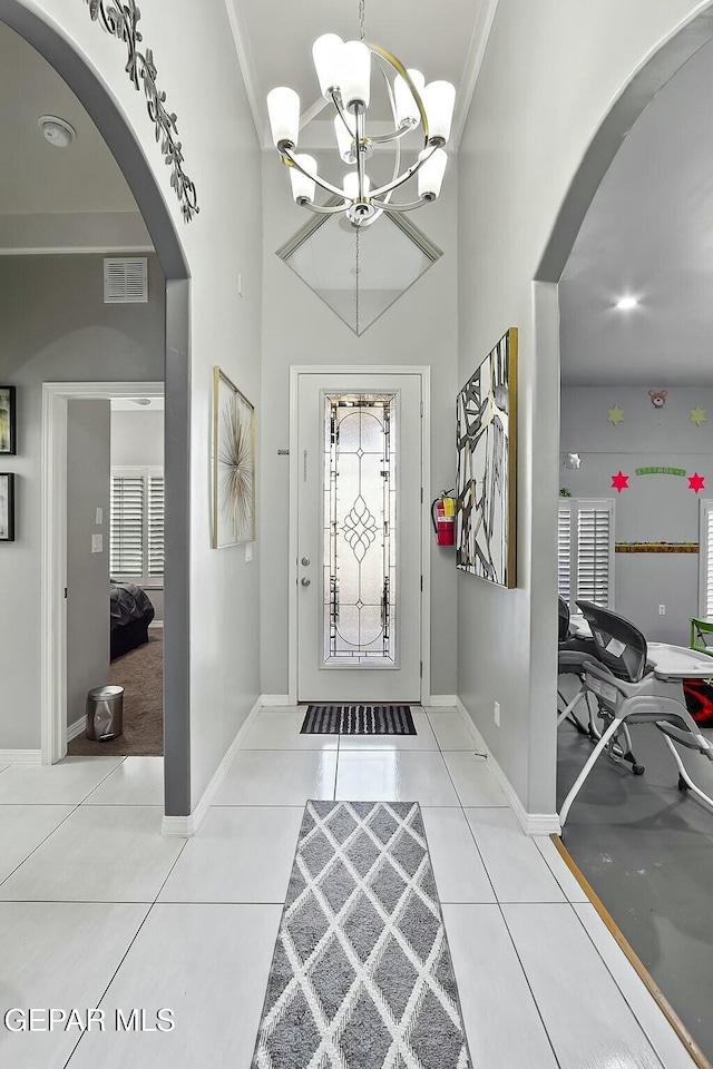 tiled entrance foyer featuring a chandelier and ornamental molding