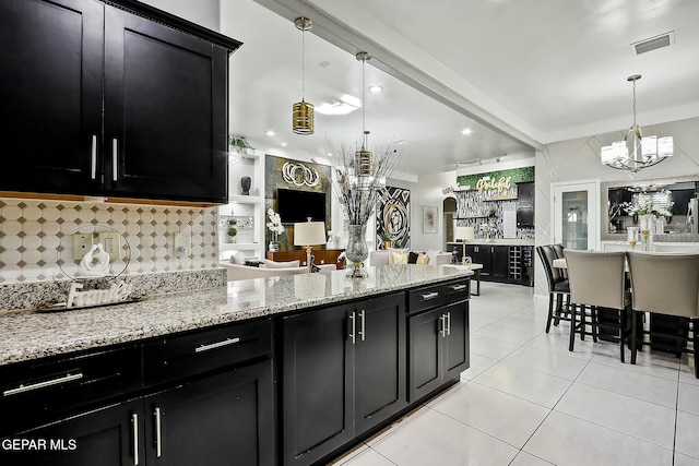 kitchen featuring light stone countertops, decorative light fixtures, decorative backsplash, a chandelier, and light tile patterned floors