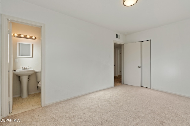 unfurnished bedroom featuring a closet, sink, light colored carpet, and ensuite bath