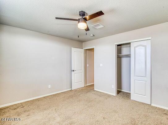 unfurnished bedroom featuring light carpet, ceiling fan, a closet, and a textured ceiling