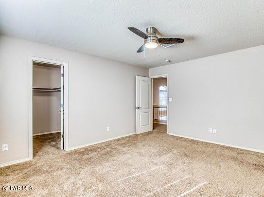 unfurnished bedroom featuring light carpet, ceiling fan, a closet, a textured ceiling, and a walk in closet