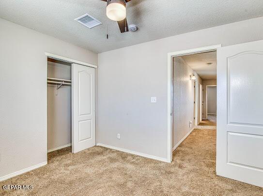 unfurnished bedroom featuring a textured ceiling, ceiling fan, a closet, and light colored carpet