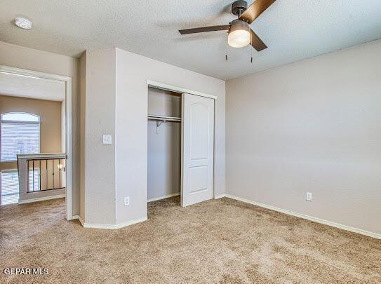 unfurnished bedroom featuring ceiling fan, a textured ceiling, a closet, and light carpet