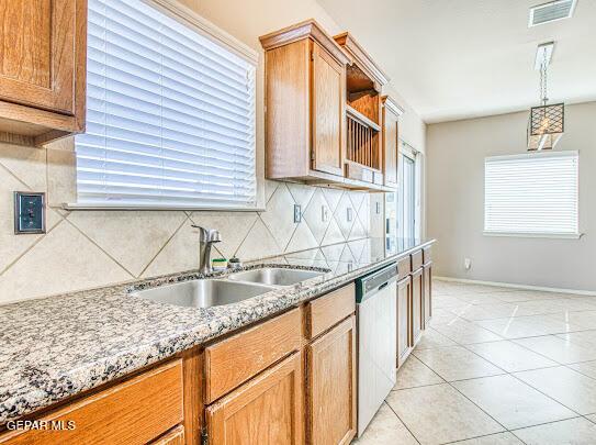 kitchen featuring light tile patterned floors, backsplash, dishwasher, light stone countertops, and sink