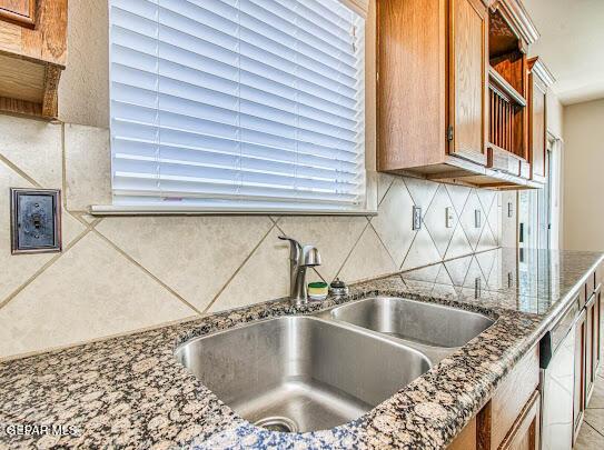 kitchen with stainless steel dishwasher, sink, stone counters, and tasteful backsplash