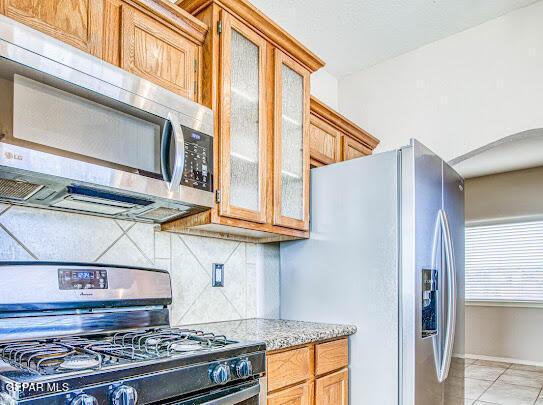 kitchen with light tile patterned flooring, appliances with stainless steel finishes, backsplash, and light stone counters