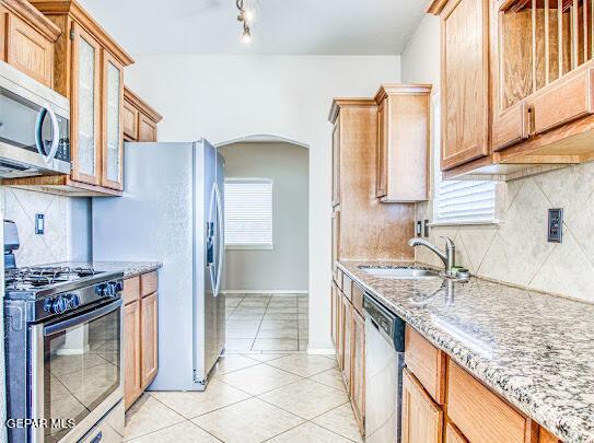 kitchen with light stone countertops, appliances with stainless steel finishes, decorative backsplash, sink, and light tile patterned flooring