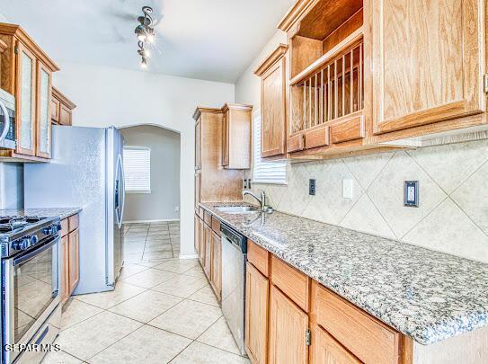 kitchen featuring stainless steel appliances, tasteful backsplash, light tile patterned flooring, light stone counters, and sink