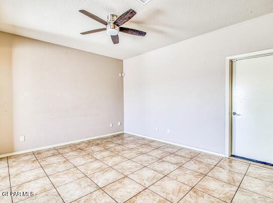 empty room featuring a textured ceiling, ceiling fan, and light tile patterned flooring