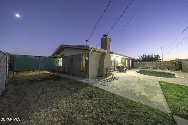 back house at dusk featuring a patio area and a fenced in pool