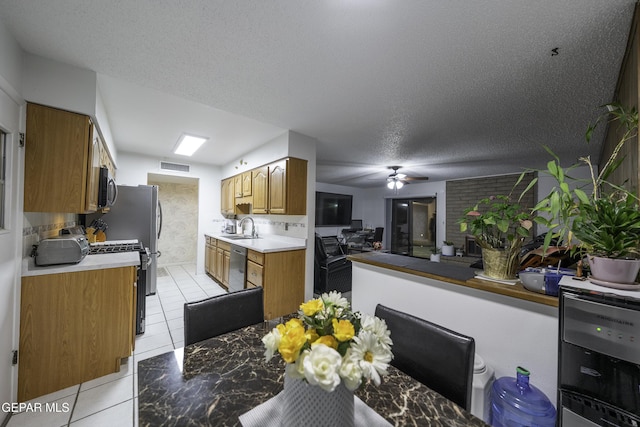 kitchen with a textured ceiling, stainless steel appliances, sink, light tile patterned flooring, and ceiling fan