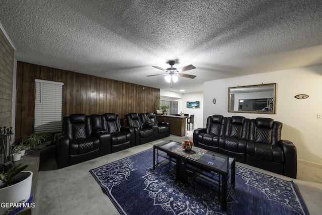 living room with a textured ceiling, ceiling fan, carpet, and wooden walls