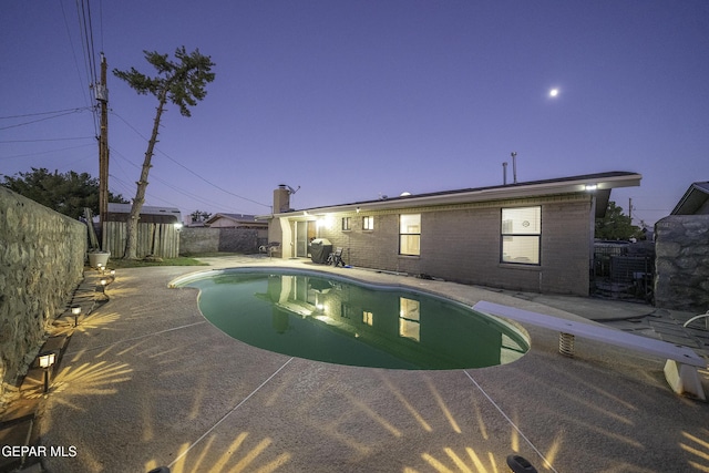 pool at dusk with a patio area and a diving board