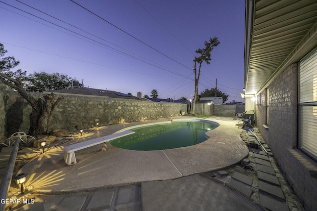 pool at dusk with a patio area and a diving board