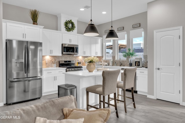 kitchen featuring decorative light fixtures, white cabinetry, backsplash, a center island, and stainless steel appliances