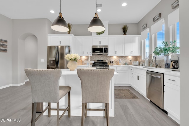 kitchen with a kitchen island, sink, white cabinets, hanging light fixtures, and stainless steel appliances