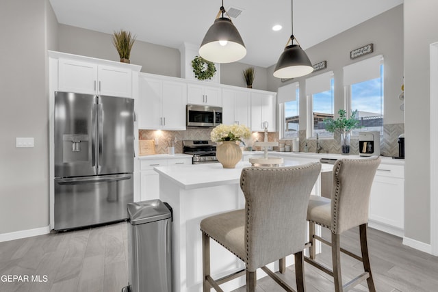 kitchen with a kitchen island, decorative light fixtures, white cabinetry, backsplash, and stainless steel appliances